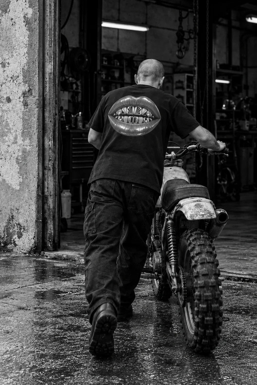 Back view of Augusta Gilded Vice black T-shirt in a monochrome motorcycle workshop editorial.
